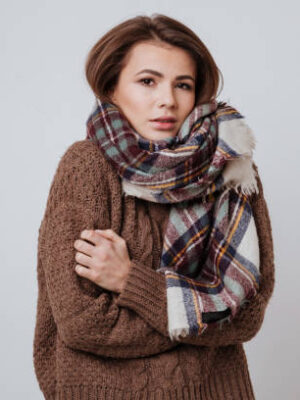 Woman in sweater and scarf freezes in studio. isolated white background