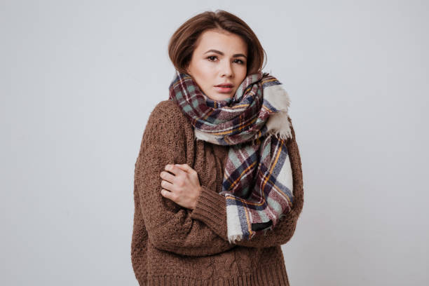 Woman in sweater and scarf freezes in studio. isolated white background
