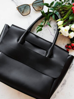 Black leather bag and flowers on a grey concrete background