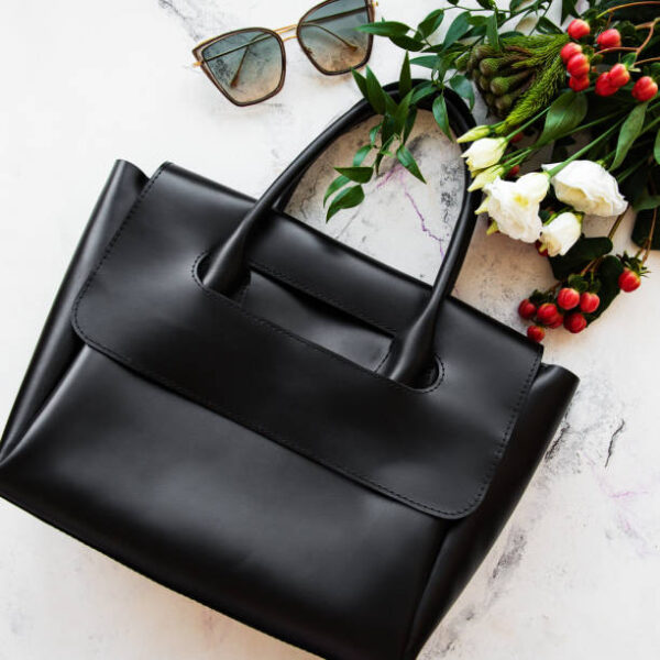 Black leather bag and flowers on a grey concrete background